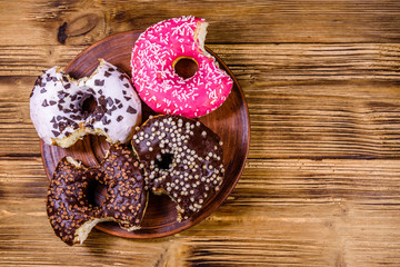 Plate with bitten glazed donuts on a wooden table. Top view