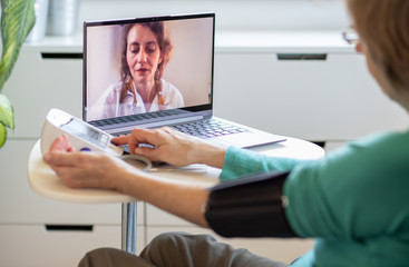 Obraz premium telemedicine concept elderly woman speaking to her doctor online and taking her blood pressure