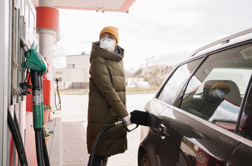 Naklejka premium Woman wearing face mask fulfilling tank in the petrol station