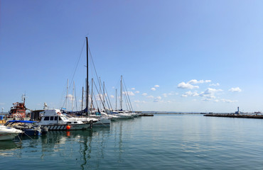 Fototapeta na wymiar Wooden pier with many yachts stand and prepare for regatta, calm sea and small clouds in the sky