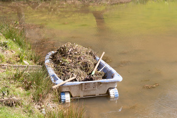 Rowing boat with weeds after cleaning the banks of a pond
