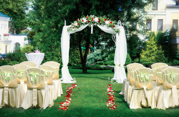 Beautiful wedding set up. Area of the wedding ceremony. Round arch, white chairs decorated with flowers, greenery. Cute, trendy rustic decor. Part of the festive decor, floral arrangement.