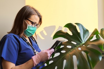Serious woman doctor in protective mask, gloves reading digital tablet