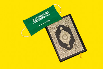 Holy Quran with Arabic calligraphy meaning of Al Quran  and Saudi Arabia flag medical mask on wood table