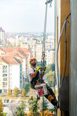 Industrial climber hanging on the rope while painting the exterior facade wall of the tall apartment building. Industrial alpinism and high risk work scene concept image