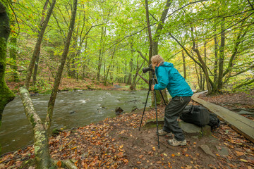 Silhouette of professional photographer taking photo of the river in forest, selective focus, long exposure