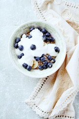 Bowl of granola with yogurt and bilberries. Concept for a tasty and healthy meal. Bright wooden background. Top view. Copy space.	