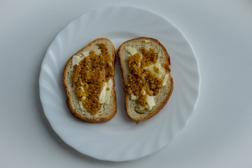 Two pieces of bread with wholegrain mustard and butter on white plate on light white background, top view