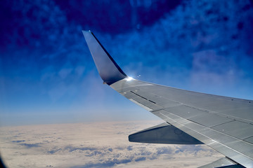 Fototapeta premium Beautiful panoramic aerial landscape - top view from the airplane window of the wing of an airplane, blue sky, clouds and the earth far below