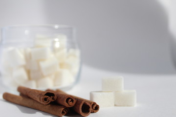 three or more sticks of cinnamon on a white background in the background is a glass jar with pieces...