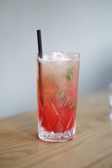 Red cocktail served in a tall cocktail glass with a straw