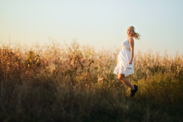 Happy woman in a white summer long dress jumping in front of the cornfield.