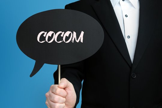 COCOM. Gesch&auml;ftsmann im Anzug h&auml;lt Sprechblase in die Kamera. Der Begriff COCOM steht im Schild. Symbol f&uuml;r Business, Finanzen, Statistik, Analyse, Wirtschaft