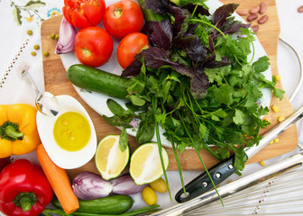 Olives on a small white bowl . Chopped green lemon. Onion . Metal whisk for whipping eggs . On a plate live tomatoes, cucumbers, chopped red onions, greens, basil, coriander on a wooden board .