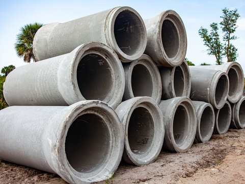 Concrete sewer pipes are stacked at a construction site, ready to be installed underground.