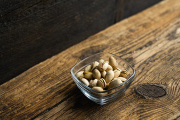 Pistachios in a small plate on a vintage wooden table as a background with a copy space. Pistachio is a healthy vegetarian protein nutritious food. Natural nuts snacks.