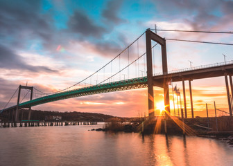 Suspension bridge at Gothenburg Connecting main land to Industrial area of Hisingen in west coast of Sweden. Setting sun creating star in between pillars of bridge - obrazy, fototapety, plakaty