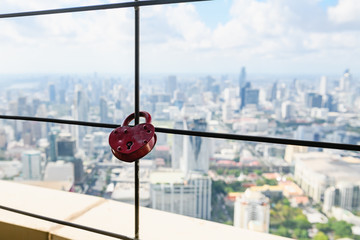 Metal red padlock fastened to big lettuce wires high up with urban city view, Thailand, Asia