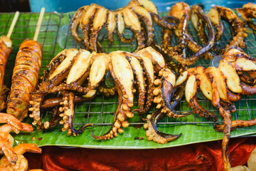 Grilled octopus tentacles, squid and other seafood at asian thai outdoor market, high protein keto snack