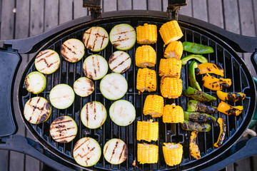 Barbeque zucchini, corn cobs and sweet bell pepper on oval grill at asian thai street food market up view