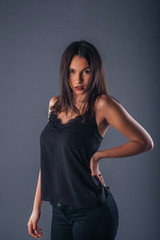 Young beautiful stylish girl posing in studio with one hand on the waist on a gray background