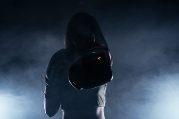 Dark contrast photo with smoke in the background of a focused strong woman with boxing gloves practicing punches