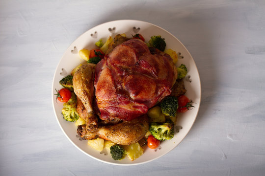 Whole roast chicken with breasts wrapped in bacon and vegetables: potatoes, broccoli and tomatoes. Overhead horizontal image
