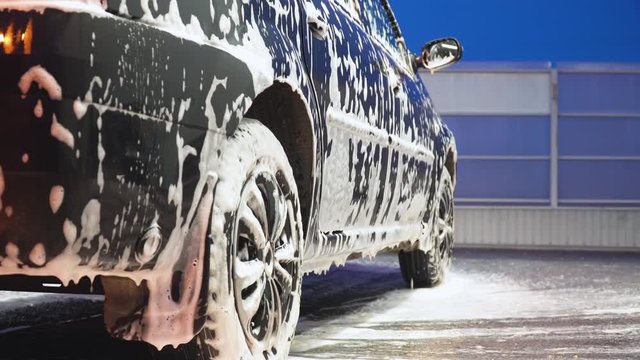 The car is covered with white washing foam. Car wash