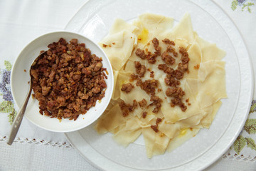 Roasted meat in a bowl . A bowl of white ceramic salt and pepper . Traditional azerbaijani khingal with force-meat on the tablecloth .