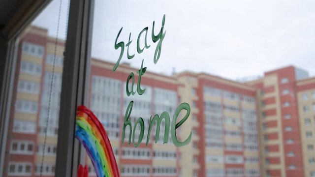 Social media campaign to prevent the covid-19 coronavirus pandemic. Drawing of a rainbow on a window during home quarantine. On the window is written : "stay at home". City view