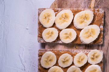 Healthy snack with crispbread, peanut butter and banana's slices on a wooden table. Top view. Close up view.
