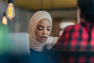 African muslim girl wearing hijab working on a laptop in a modern startup company.