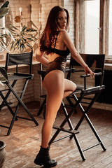 Fototapeta na wymiar Sensual young female model with dark hair and erotic lingerie posing in a bright room filled with sunlight showing her curves
