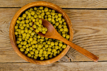 Fototapeta na wymiar Wooden bowl with canned green peas on table.