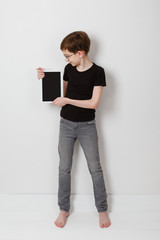 A boy teenager is browsing at his laptop copy space, full height portrait on white background. Sitting at home in casual outfit. Distance learning. Internet technology in schoolboy's life. Gamer child