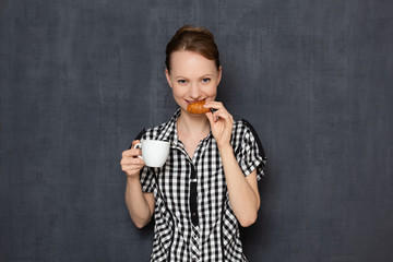 Portrait of happy girl holding coffee cup and croissant in hands