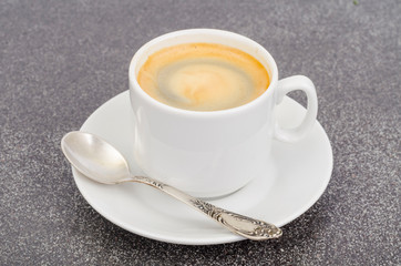 White cup espresso with foam on gray stone background.