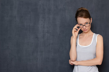 Portrait of focused young woman, attentively looking over her glasses