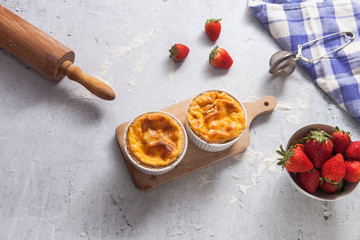 Home made creme brulee dessert or 
custard tarts with strawberries and fresh mint leaves on a light grey concrete background with  bowl  of strawberries,  a sifter and a table cloth. Copy space.