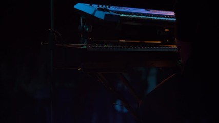 Man's hand playing a song on the electric keyboard piano at a concert in dark atmospheric light - 4k close up