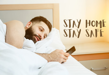 Bearded man lying in morning bed with phone using app or reading news feed