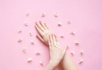 Naklejka na ściany i meble Hands of a woman with white flowers on a pink background. Natural cosmetics product and hand care, moisturizing and wrinkle reduction. Flat Lay and skincare concept.