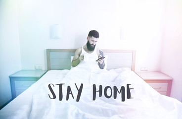Bearded man lying in bed with morning coffee and phone using app or reading news