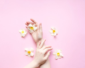 Obraz na płótnie Canvas Hands and flowers are on a pink background. Natural Cosmetics for hand skin care, a means to reduce wrinkles on hands, moisturizing. Natural cosmetics from flower extract, beauty and fashion
