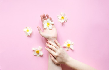 Hands and  flowers are on a pink background. Natural Cosmetics for hand skin care, a means to reduce wrinkles on hands, moisturizing. Natural cosmetics from flower extract, beauty and fashion