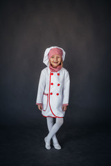 little girl in a white chef uniform on a dark background