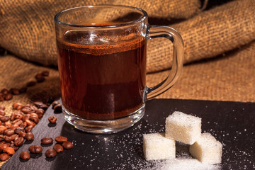 black coffee in a transparent glass Cup on a background of burlap. next to sugar, coffee beans and ground coffee. vintage
