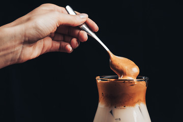 girl mixes Iced korean Dalgona Coffee with a spoon, a trendy fluffy creamy whipped coffee with ice. trendy coffee drink