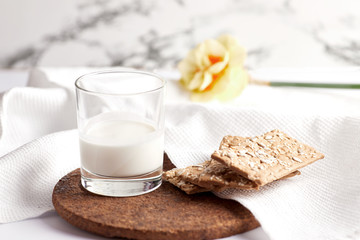 Milk in a transparent glass and healthy cookies with cereals on a cork wood stand. On a marble background.