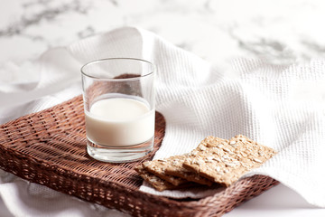 Milk in a transparent glass and healthy cookies with cereals on a cork wood stand. On a marble background.
